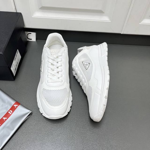 Prada 男士新款织物网眼系带运动鞋 这款采用轻质磨砂Tpu拼接透气织物网眼鞋面，轻盈透气，柔软舒适，富有现代特色。外侧饰以标志性三角金属珐琅徽标，后跟小牛皮