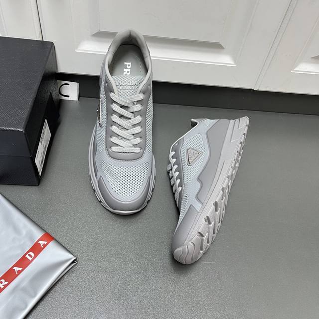 Prada 男士新款织物网眼系带运动鞋 这款采用轻质磨砂Tpu拼接透气织物网眼鞋面，轻盈透气，柔软舒适，富有现代特色。外侧饰以标志性三角金属珐琅徽标，后跟小牛皮
