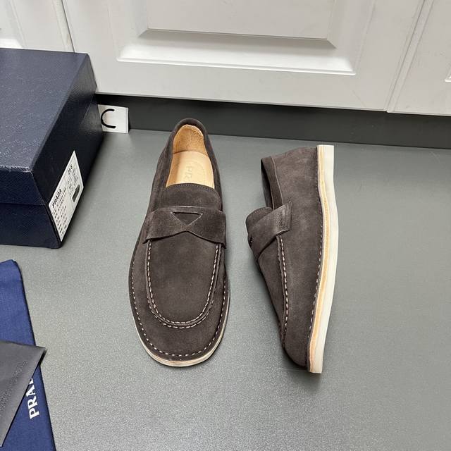 Prada 男士新款绒面皮革乐福鞋 这款采用植绒面牛二层皮革打造，结合经典设计与手工细节，将精致气息与休闲惬意融为一体。外侧烫印Logo徽标，裙饰拼接明线接缝，