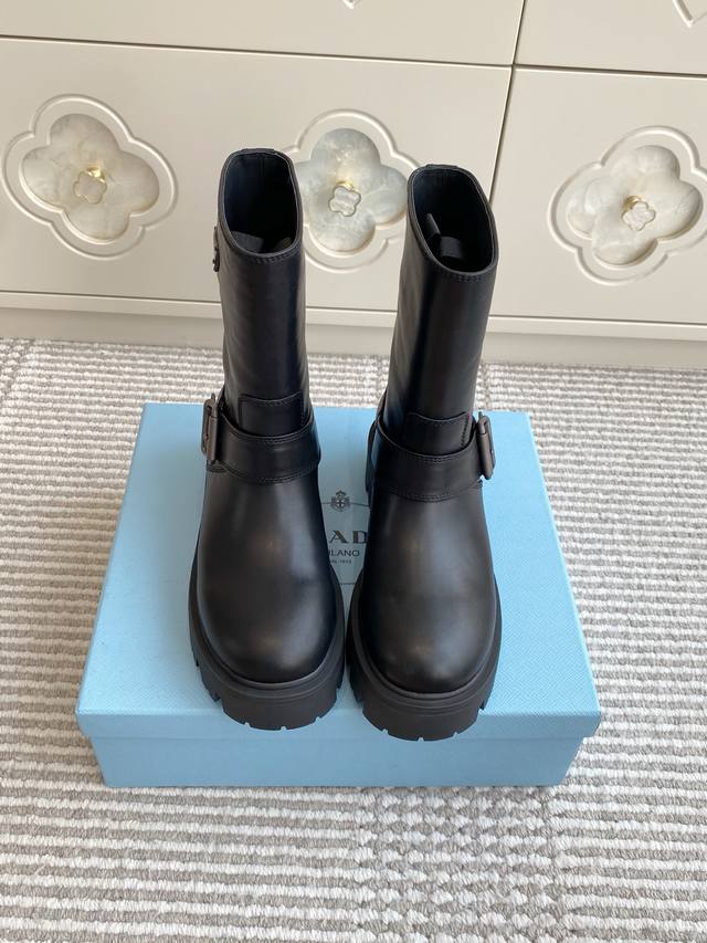 批羊京 牛皮 Prada普拉达新款厚底机车靴 短靴 顶级品质 精致线条与工艺构造定义此款皮革短靴，饰有标志性三角形徽标。独特的金属搭扣为机车风格增添个性，搭配厚