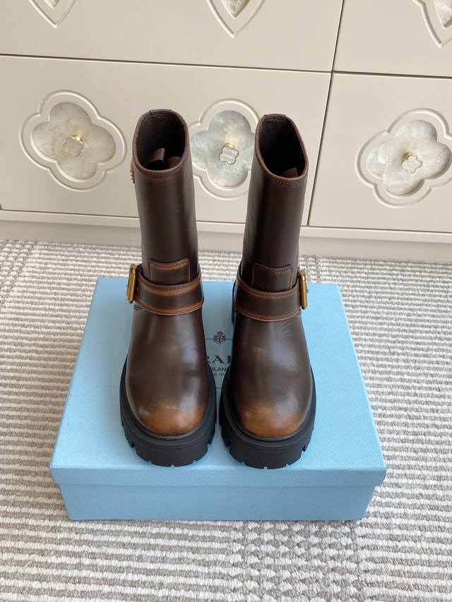 批羊京 牛皮 Prada普拉达新款厚底机车靴 短靴 顶级品质 精致线条与工艺构造定义此款皮革短靴，饰有标志性三角形徽标。独特的金属搭扣为机车风格增添个性，搭配厚