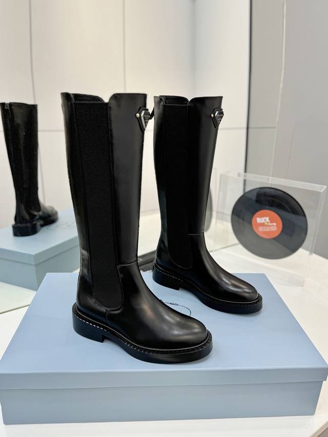 工厂p价 普拉达短靴 秋冬新款prada普拉达三角钻形扣短筒切尔西 这款鞋履配有鲜明的圆形鞋头，橡胶厚底为经典乐福鞋注入现代外观，涂珐琅金属徽标装饰彰显品牌格调