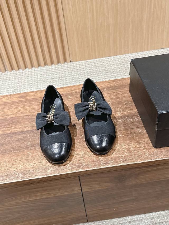 Chanel 香奈儿蝴蝶结平底单鞋 采用圆头设计，鞋头部分为亮面皮革，鞋身主体为黑色织物材质，拼接设计富有层次感；鞋面上装饰有大尺寸蝴蝶结，蝴蝶结中央搭配金属链