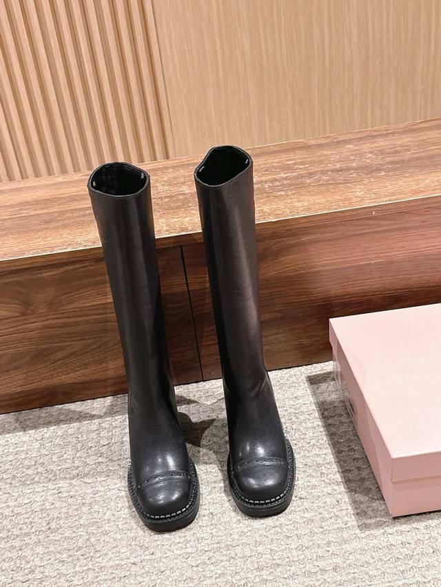 代购级 Miu Miu 缪缪新品甜酷风黑色粗跟高筒靴长靴 DDD DDD 经典高筒靴型，搭配圆头+粗跟厚底，鞋头有布洛克雕花细节，靴筒边缘的银色缝线装饰是亮点，