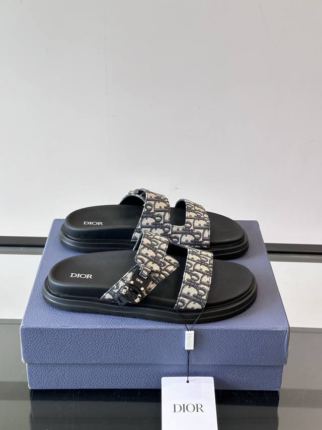 Dior Aqua 男士凉鞋拖鞋。展现 Dior 高订风格设计。迪奥灰绒面革饰带点缀以铝质 Dior 搭扣提升格调。搭配舒适的同色调凹口鞋底，可与短裤或牛仔裤轻